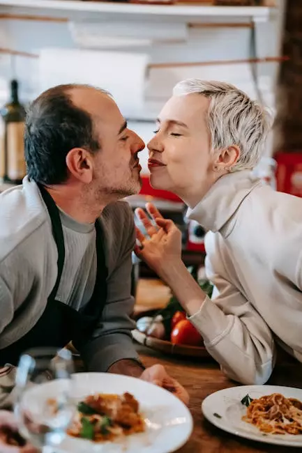 Loving couple leaning towards each other, about to share a kiss, with freshly cooked dishes placed on the kitchen table.