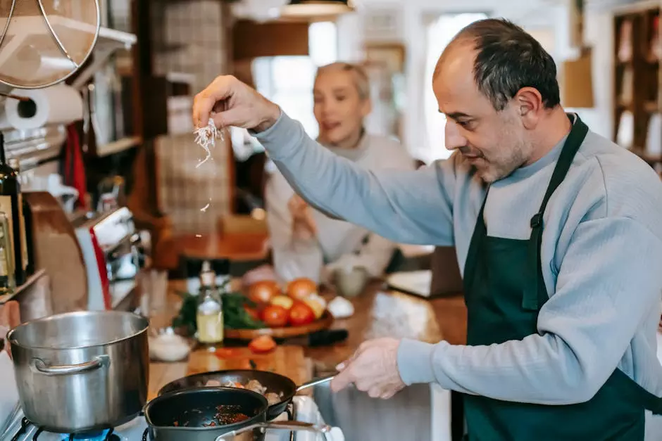 Man cooking in a cozy kitchen, carefully sprinkling cheese into a pan, while his partner chats happily in the background.